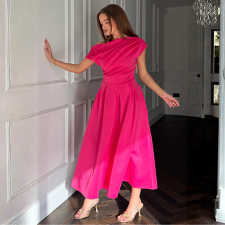 Woman in a bright pink dress standing in a room with white paneled walls.