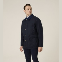 Load image into Gallery viewer, A man wearing a dark navy blue jacket with gold buttons and matching navy trousers, standing against a plain light beige studio background.
