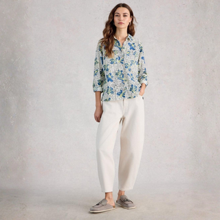 Woman wearing a patterned shirt and white pants against a plain background