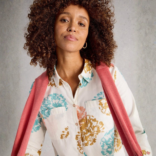 Woman wearing a floral blouse with a pink shawl over her shoulders against a gray background