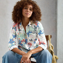 Load image into Gallery viewer, Woman wearing a floral shirt sitting on a chair against a gray wall.
