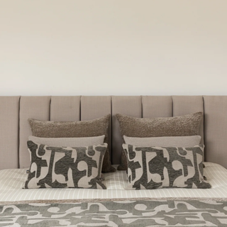 Bed with patterned pillows and a neutral headboard against a beige wall.