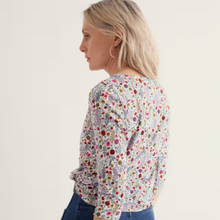 Load image into Gallery viewer, A woman shown from the side/back wearing a long-sleeve blouse with a dense multicolor floral and paisley print on a white base, paired with blue jeans against a plain off-white studio background.
