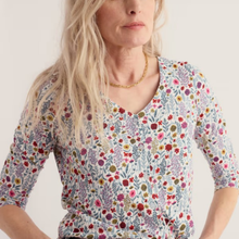 Load image into Gallery viewer, A woman wearing a short-sleeve V-neck top with a dense multicolor floral and botanical print on a light background, paired with a gold chain necklace.
