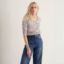Load image into Gallery viewer, A woman modeling a short-sleeve floral print top with blue jeans and a black belt, standing against a plain off-white background.
