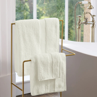 Almond towels hanging on a gold towel rack in a bathroom with a window in the background.