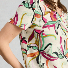 Load image into Gallery viewer, A close-up of a woman wearing a short-sleeve V-neck top with a colorful abstract floral print on a cream background.
