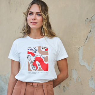 Woman wearing a white t-shirt with a graphic design against a textured wall.