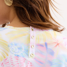 Load image into Gallery viewer, Close-up of a colorful tie-dye shirt with gold buttons on a blurred background
