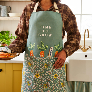 Person wearing a green apron with 'Time to Grow' text in a kitchen.