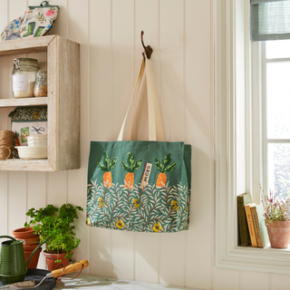 Green tote bag with carrot design hanging on a hook next to a window
