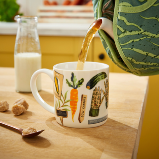 Time to Grow Muff Tea Cozy pouring into a mug, with a colorful kitchen background.