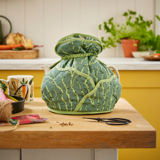 Front view of Time to Grow Muff Tea Cozy, with a colorful kitchen background.