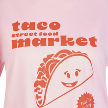 Load image into Gallery viewer, Pink t-shirt with a smiling taco graphic and 'taco street food market' text on a pink background
