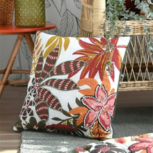 Load image into Gallery viewer, A square throw pillow with a vibrant tropical floral pattern in red, orange, brown, and green on a white background, styled in a home setting on a gray rug.

