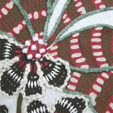 Load image into Gallery viewer, Close-up of a textile pattern with embroidered floral motifs in red, olive green, white, and black on a woven fabric background.
