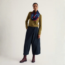 Load image into Gallery viewer, A model stands against a plain off-white studio background wearing a mustard green cardigan, dark navy wide-leg cropped trousers, a blue and red patterned infinity scarf, and dark burgundy ankle boots.
