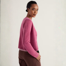 Load image into Gallery viewer, A woman wearing a fuzzy pink cropped cardigan sweater and brown trousers, photographed against a plain off-white studio background.
