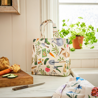 Tote bag with gardening-themed design on a kitchen counter with vegetables and plants.