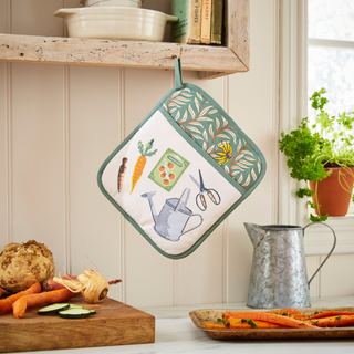 Potholder with gardening illustrations hanging on a wooden shelf with vegetables and a watering can.