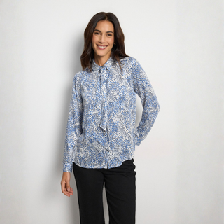 A woman modeling a light blue and white patterned long-sleeve blouse with a tie-neck detail, paired with black pants, against a plain light gray background.