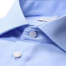 Load image into Gallery viewer, Close-up of a light blue dress shirt collar with white buttons, showing the fine twill fabric texture and a partially visible neck label.
