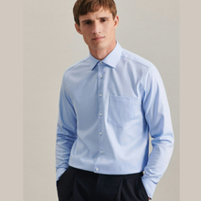 Load image into Gallery viewer, A man wearing a light blue long-sleeve dress shirt with a classic collar and chest pocket, paired with dark trousers, set against a plain light gray background.
