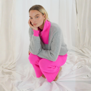 Person wearing a gray and pink outfit sitting on a white fabric background