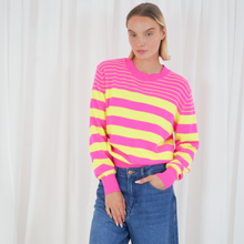 Load image into Gallery viewer, Person wearing a pink and yellow striped sweater with blue jeans against a white curtain background
