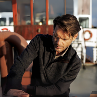 Man sitting on a boat looking down with a serious expression