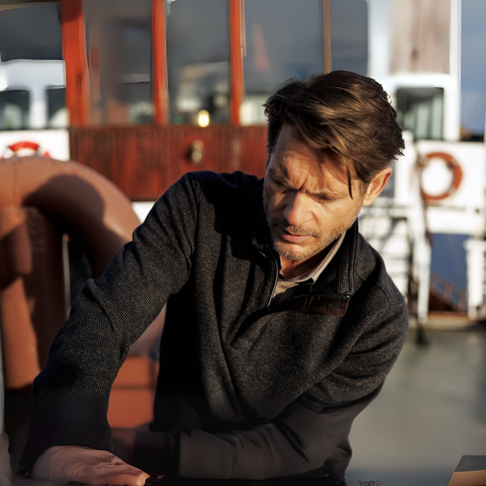 Man sitting on a boat looking down with a serious expression