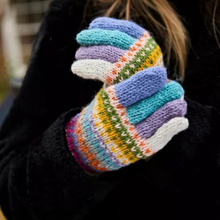Load image into Gallery viewer, A close-up of a person wearing a pair of hand-knit winter gloves with a multicolor Fair Isle pattern of blue, purple, teal, green, orange, and white, worn over a black coat.
