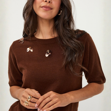 Load image into Gallery viewer, A woman wearing a brown short-sleeve knit sweater with decorative metallic flower embellishments on the chest, photographed against a plain light background.
