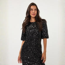 Load image into Gallery viewer, A woman wearing a black sequined short-sleeve dress, standing against a plain off-white background.
