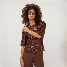 Load image into Gallery viewer, A woman with curly hair wearing a brown sequined short-sleeve top and matching brown pants, standing against a plain light gray background.

