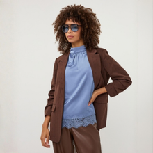 Load image into Gallery viewer, A model with curly hair wearing a brown textured blazer, a light blue high-neck blouse with lace trim, and brown pants, styled with blue-tinted sunglasses against a plain white background.
