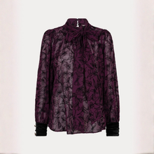 Load image into Gallery viewer, A sheer long-sleeve blouse in deep purple with a black floral pattern, featuring a high mock neck with a bow, gathered shoulders, and black ruffled cuffs.
