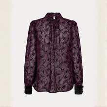 Load image into Gallery viewer, A sheer, long-sleeve blouse in deep purple with a black floral line-art pattern, featuring a high mock neck and black ruffled cuffs, shown against a plain off-white background.
