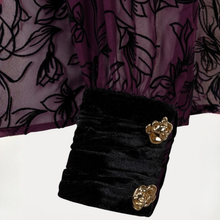Load image into Gallery viewer, Close-up of a black velvet sleeve cuff with two gold rose-shaped buttons, paired with a sheer purple floral tulle fabric.

