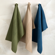 Load image into Gallery viewer, Three folded towels in green, beige, and blue hanging on a white textured surface.
