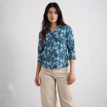 Load image into Gallery viewer, A woman modeling a blue floral button-up shirt with three-quarter sleeves and beige pants, standing against a plain light gray studio background.
