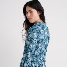 Load image into Gallery viewer, A woman wearing a blue long-sleeve button-up shirt with a white and brown floral pattern, photographed against a plain light gray background.
