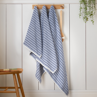 Two blue and white striped towels hanging on a wooden rack against a white wall.