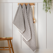 Load image into Gallery viewer, Striped towel hanging on a wooden rack against a white paneled wall.
