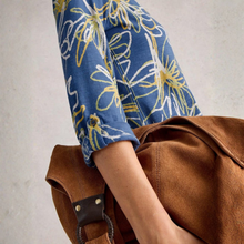 Load image into Gallery viewer, Person wearing a blue floral shirt with rolled-up sleeves, sitting on a brown bag against a neutral background
