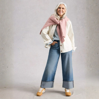 Woman wearing a white coat, pink scarf, blue jeans, and beige shoes against a gray background