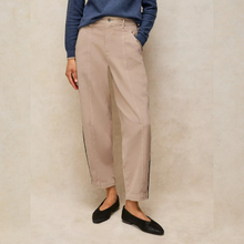 Load image into Gallery viewer, A person wearing beige straight-leg pants with black side stripes, paired with a blue long-sleeve top and black flats, standing against a textured beige wall.
