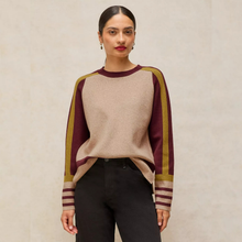 Load image into Gallery viewer, A woman modeling a long-sleeve knit sweater with a beige body and maroon and olive green raglan sleeves, paired with black pants against a neutral beige background.
