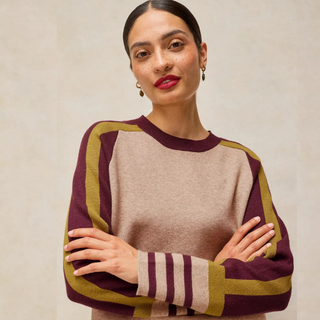 A woman modeling a long-sleeve knit sweater with a beige body and maroon and olive green raglan sleeves