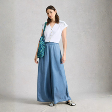 Load image into Gallery viewer, Woman wearing a white blouse and blue denim skirt holding a green bag against a plain background
